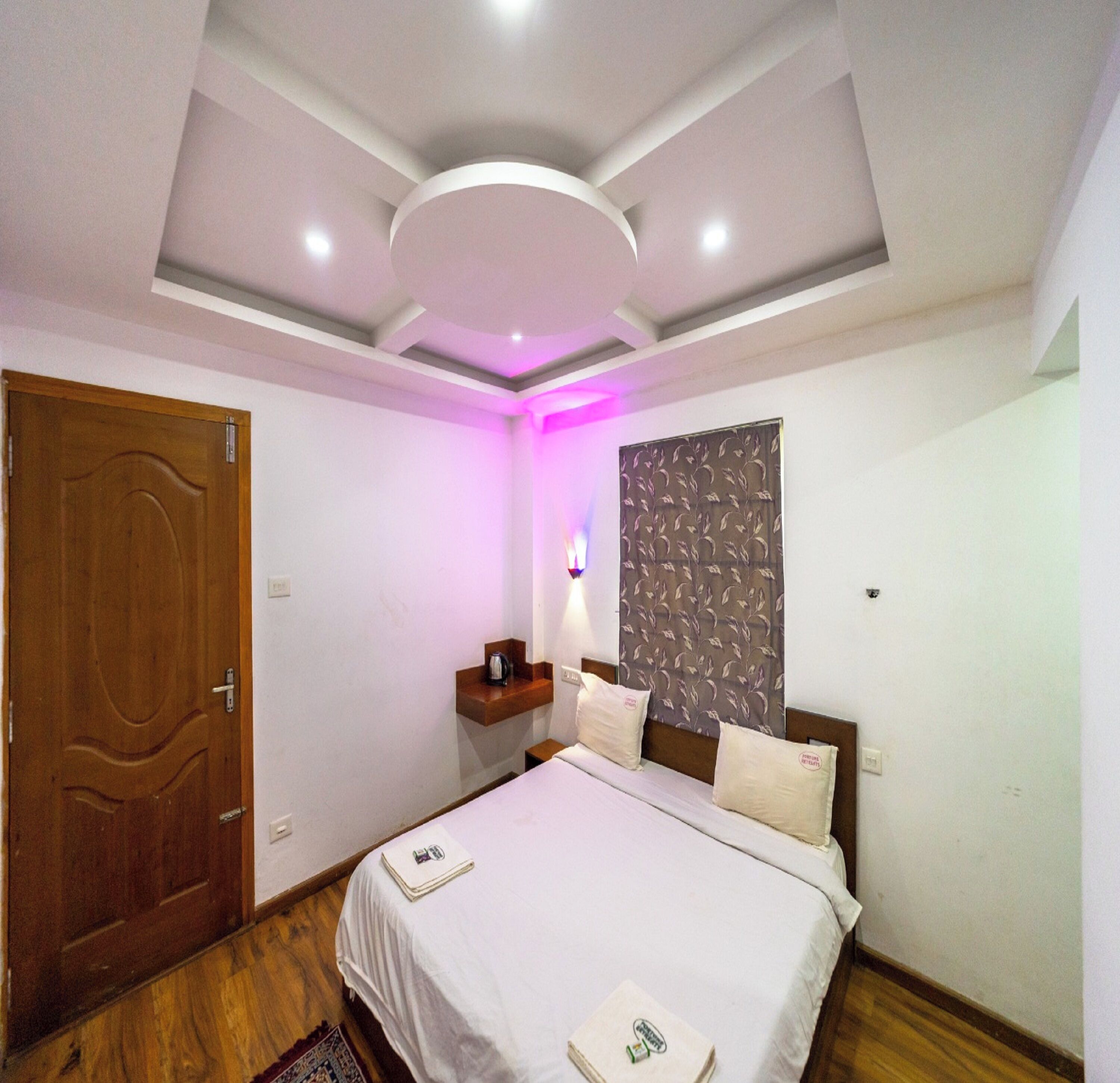 Una camera da letto con un letto, una porta in legno, un comodino e un punto luce a parete.