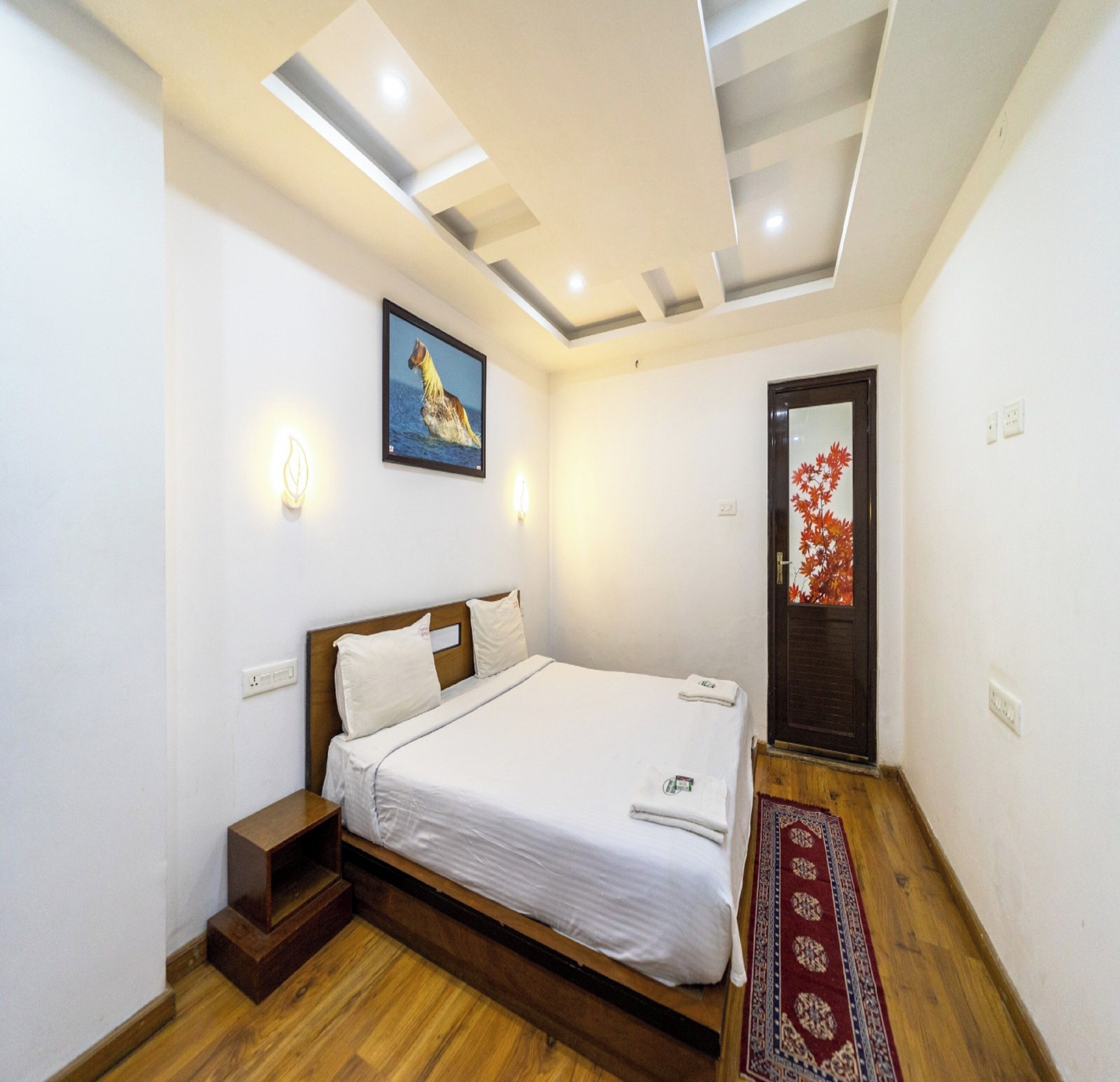 Une chambre à coucher avec un lit en bois, un tableau représentant un cheval, un tapis rouge et une porte ornée d’un motif de feuilles rouges.