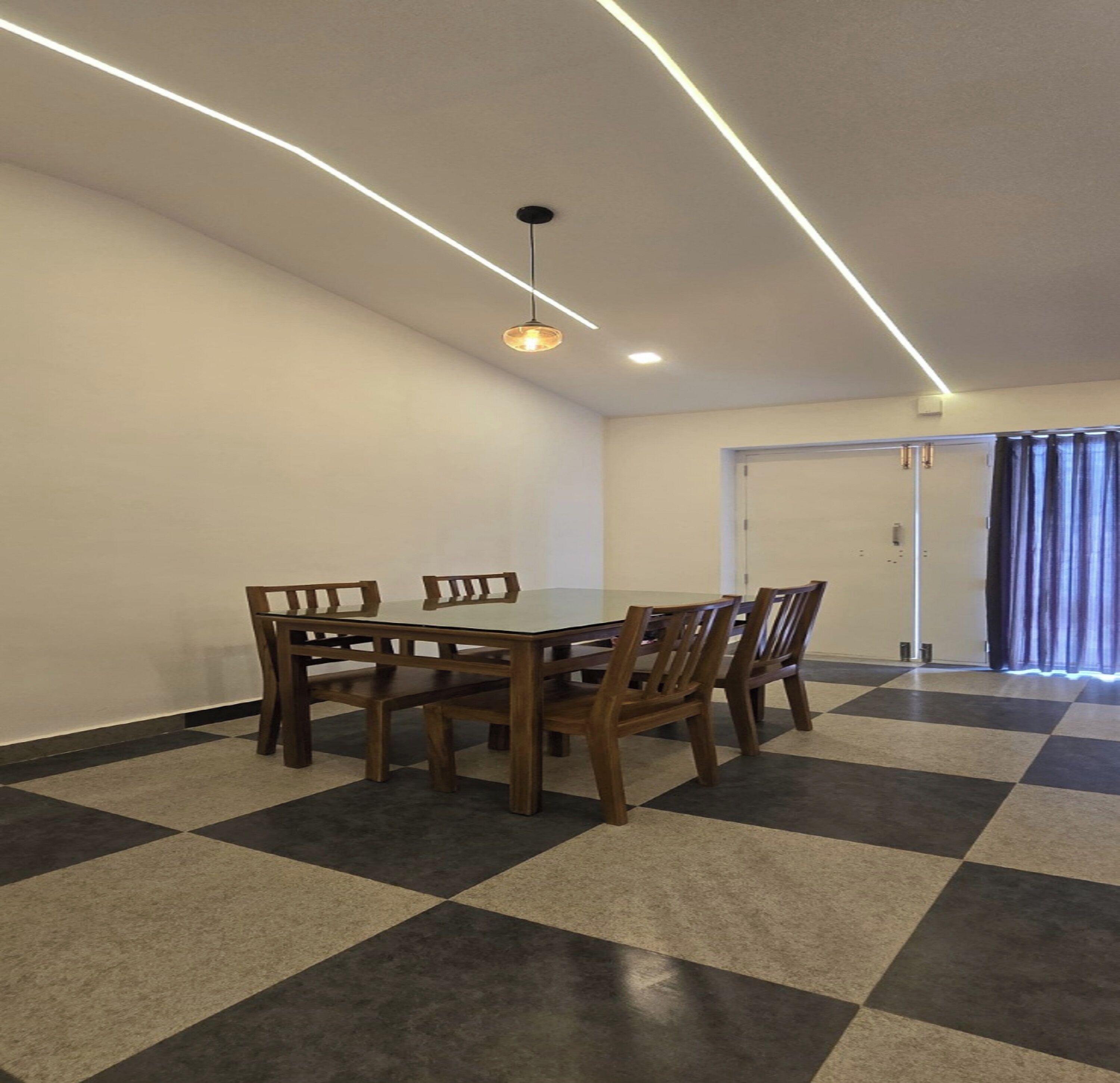 A dining area with a checkered floor, a wooden table, and chairs. There is a ceiling light fixture above the table.