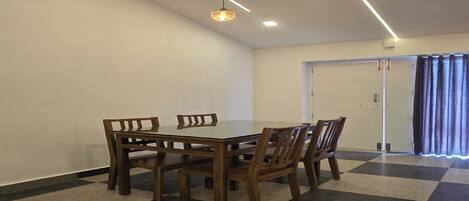 A dining area with a checkered floor, a wooden table, and chairs. There is a ceiling light fixture above the table.
