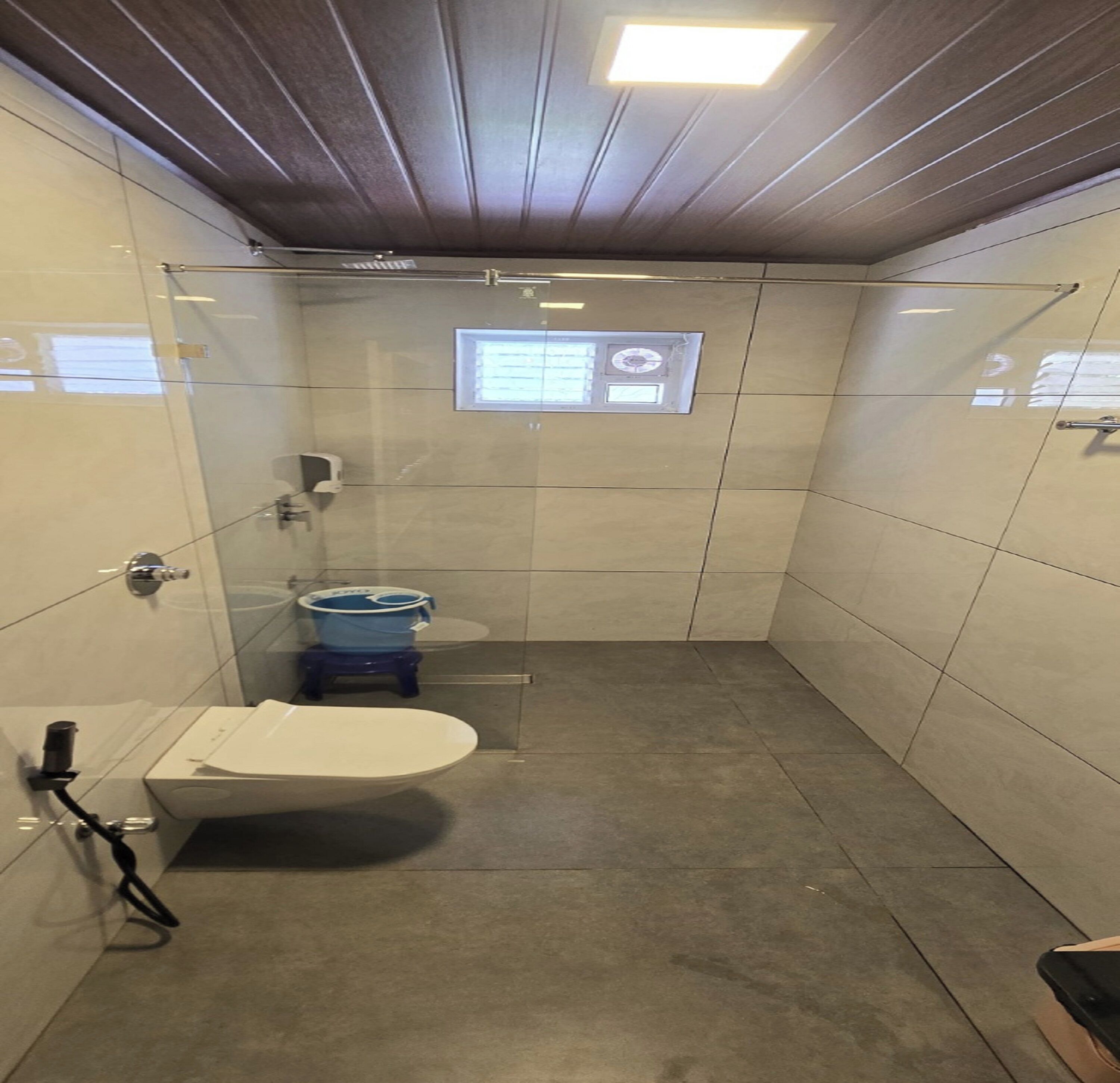 Une petite salle de bain carrelée, équipée de toilettes, d’un sèche-mains et d’une fenêtre avec une horloge.
