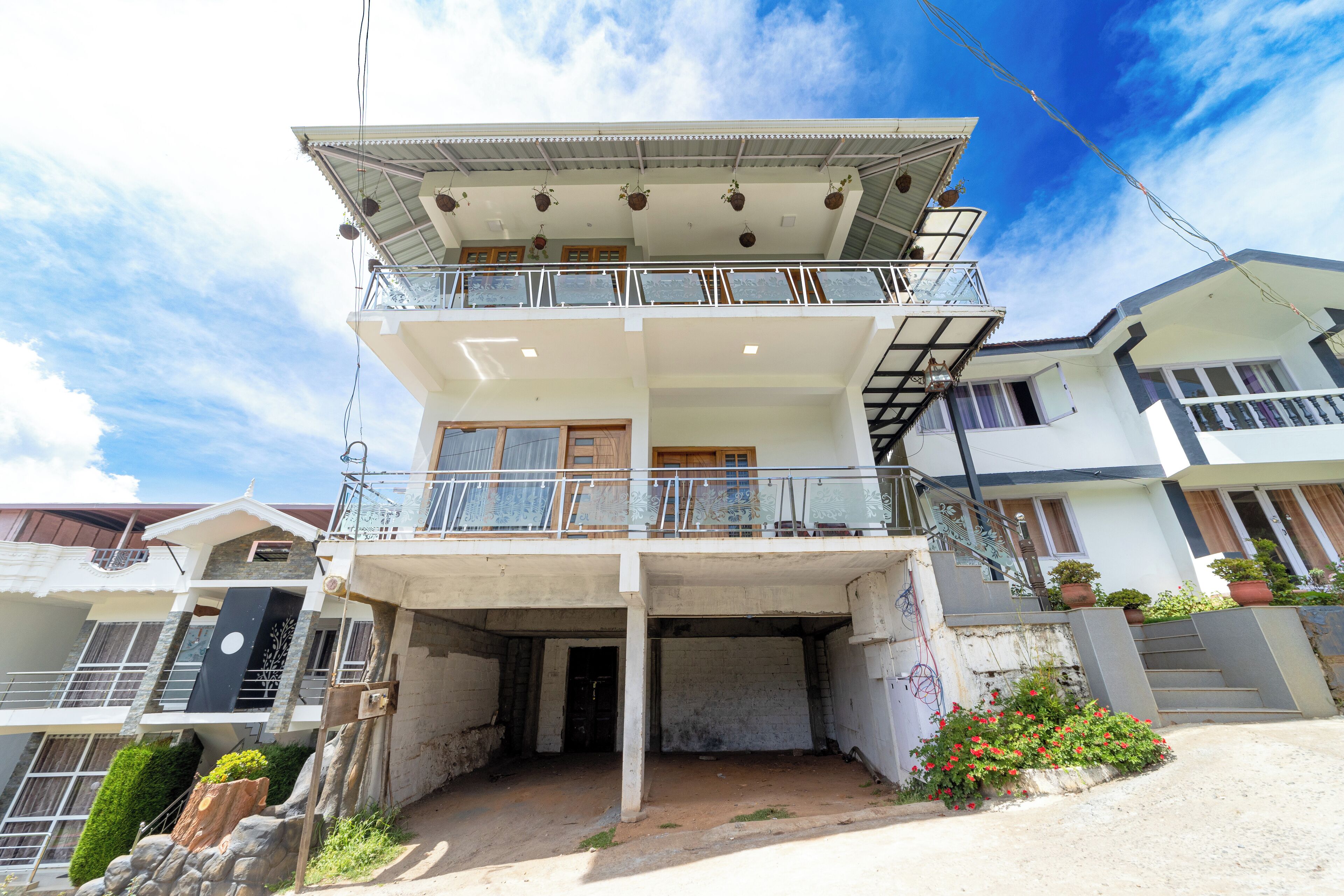 A multi-story building with a balcony on the upper floor, a staircase leading to the entrance, and a small garden area with flowers.