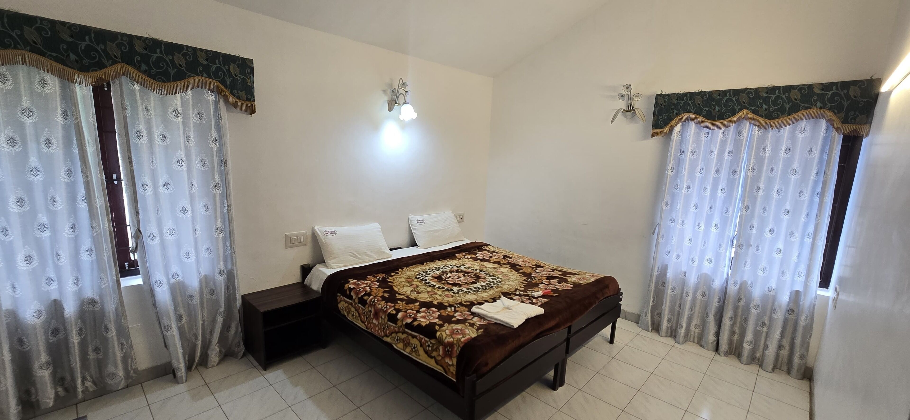 A bedroom with a bed, curtains, a nightstand, and wall sconces.