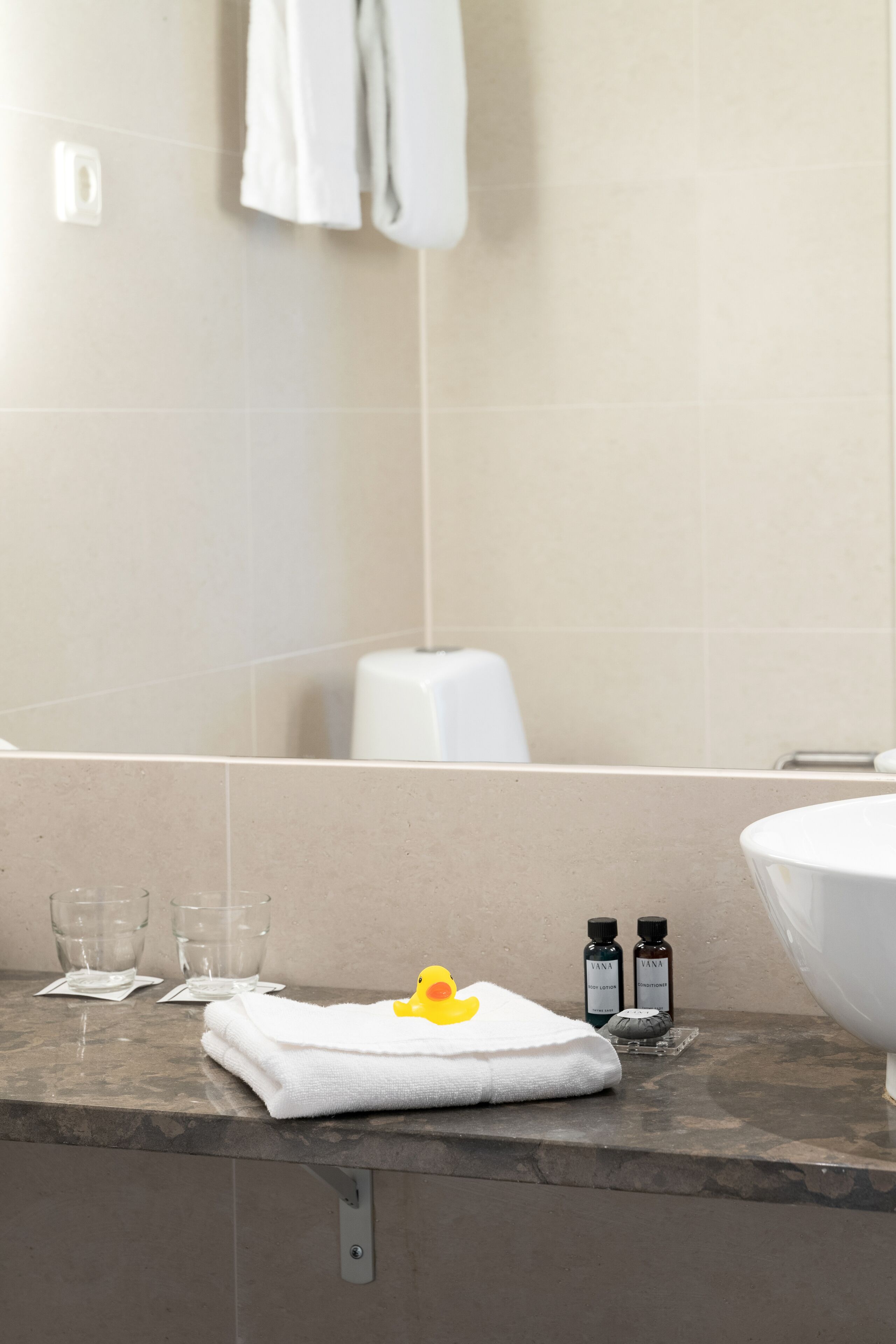 A bathroom with a marble countertop, a white towel, two small bottles, and a glass.