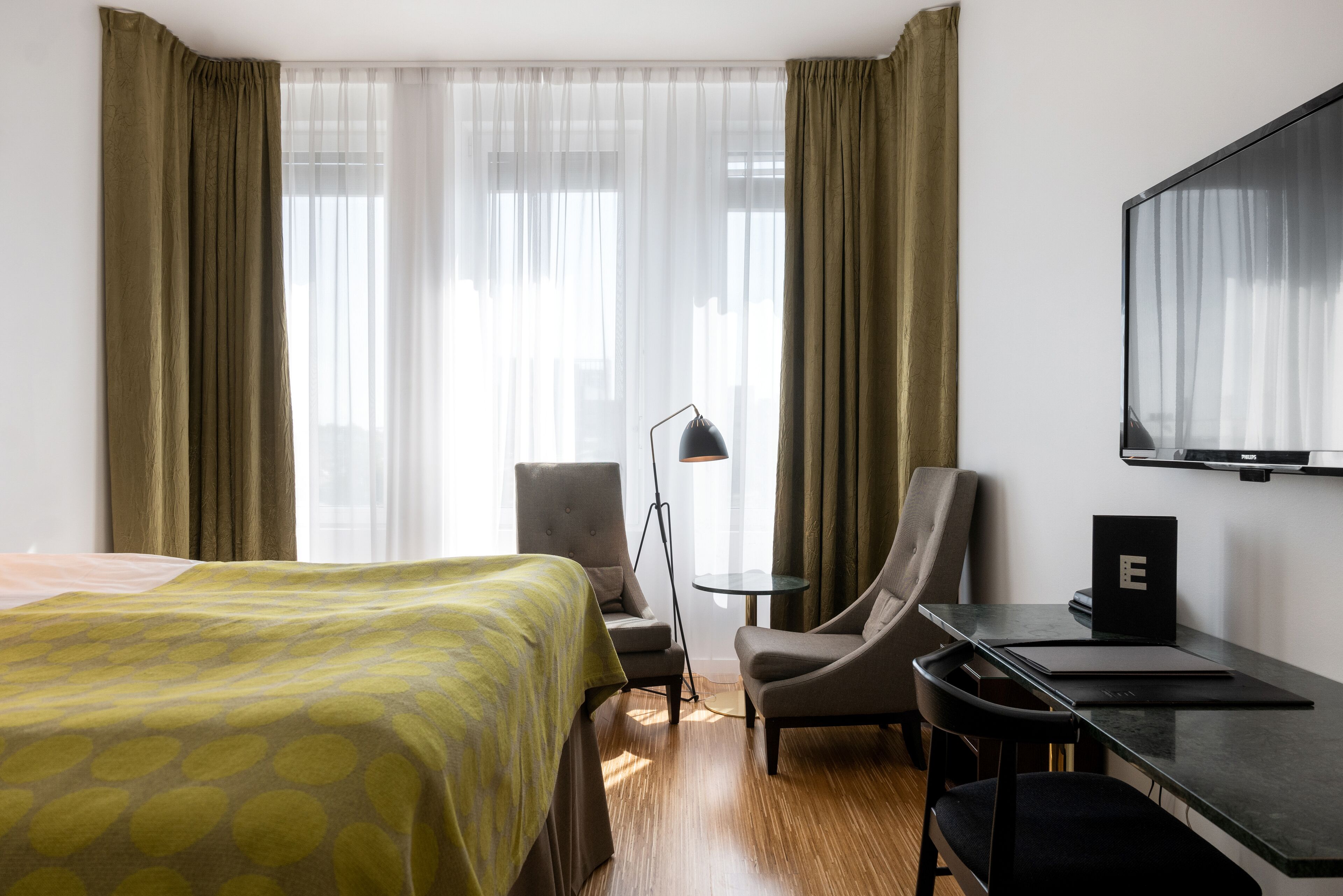 Une chambre d’hôtel avec un lit, un bureau avec un ordinateur portable, une chaise et un téléviseur fixé au mur.