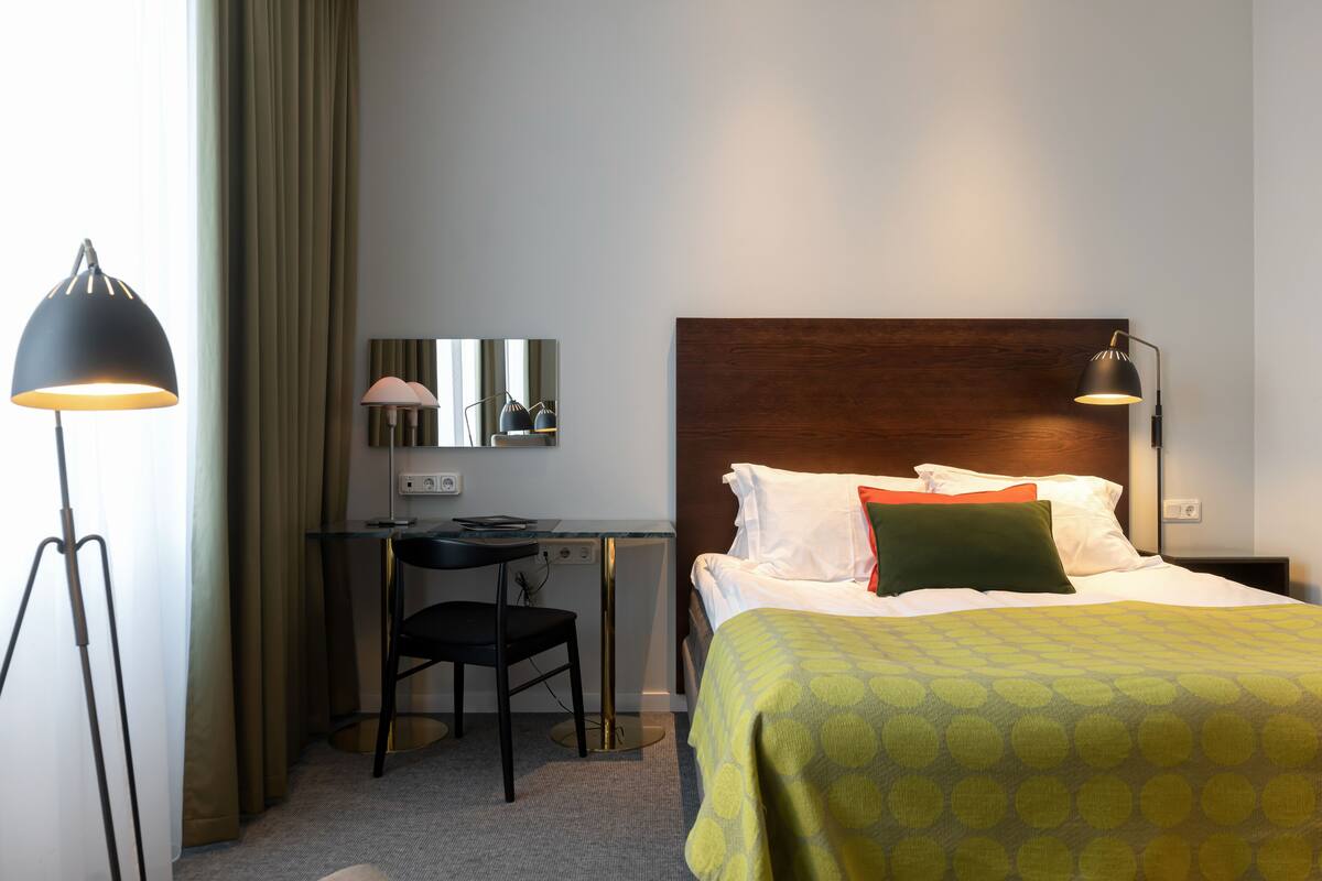 Ett hotellrum med en säng, ett skrivbord, en stol och två lampor.