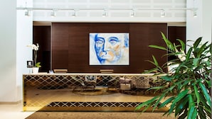 Un área de recepción moderna con un gran cuadro abstracto, un mostrador de recepción, zona de estar y una planta grande.