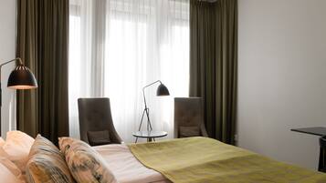 Quarto de hotel com cama, duas poltronas, uma mesinha e um abajur.