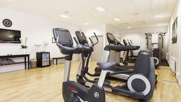 Ein Fitnessraum mit Cardiogeräten, einem Fernseher und einer Wanduhr.