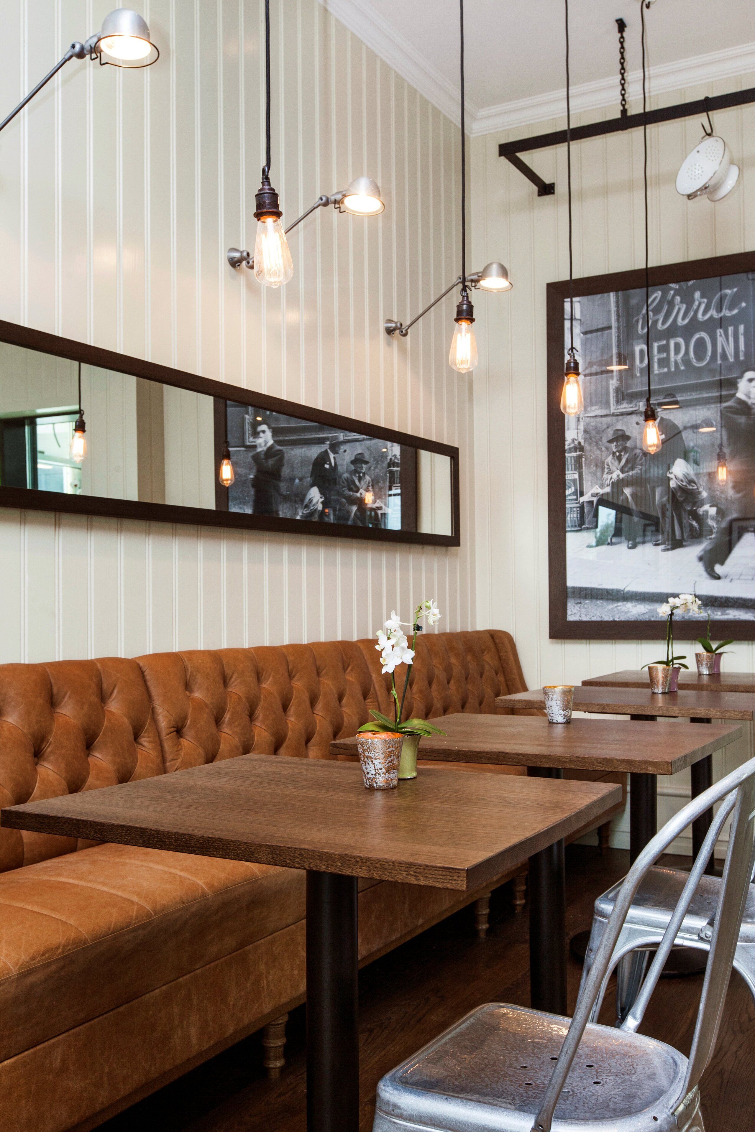En restauranginteriör med en träbänk som sittplats, ett bord med stolar, hängande lampor och ett inramat svartvitt fotografi på väggen.