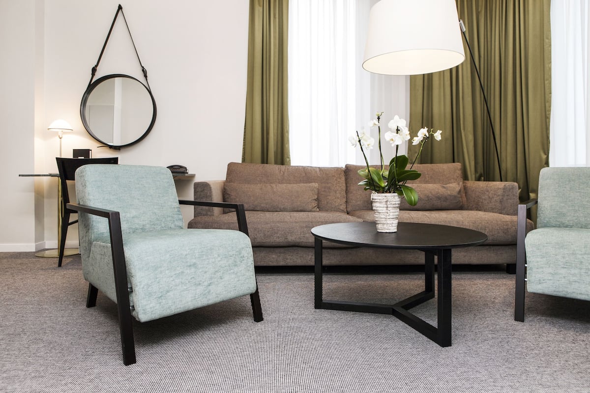 Ett modernt vardagsrum med en soffa, två fåtöljer, ett soffbord, en rund spegel och en lampa.