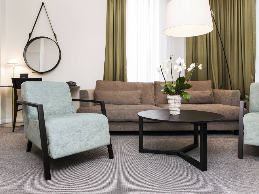 A modern living room with a sofa, two armchairs, a coffee table, a round mirror, and a lamp.