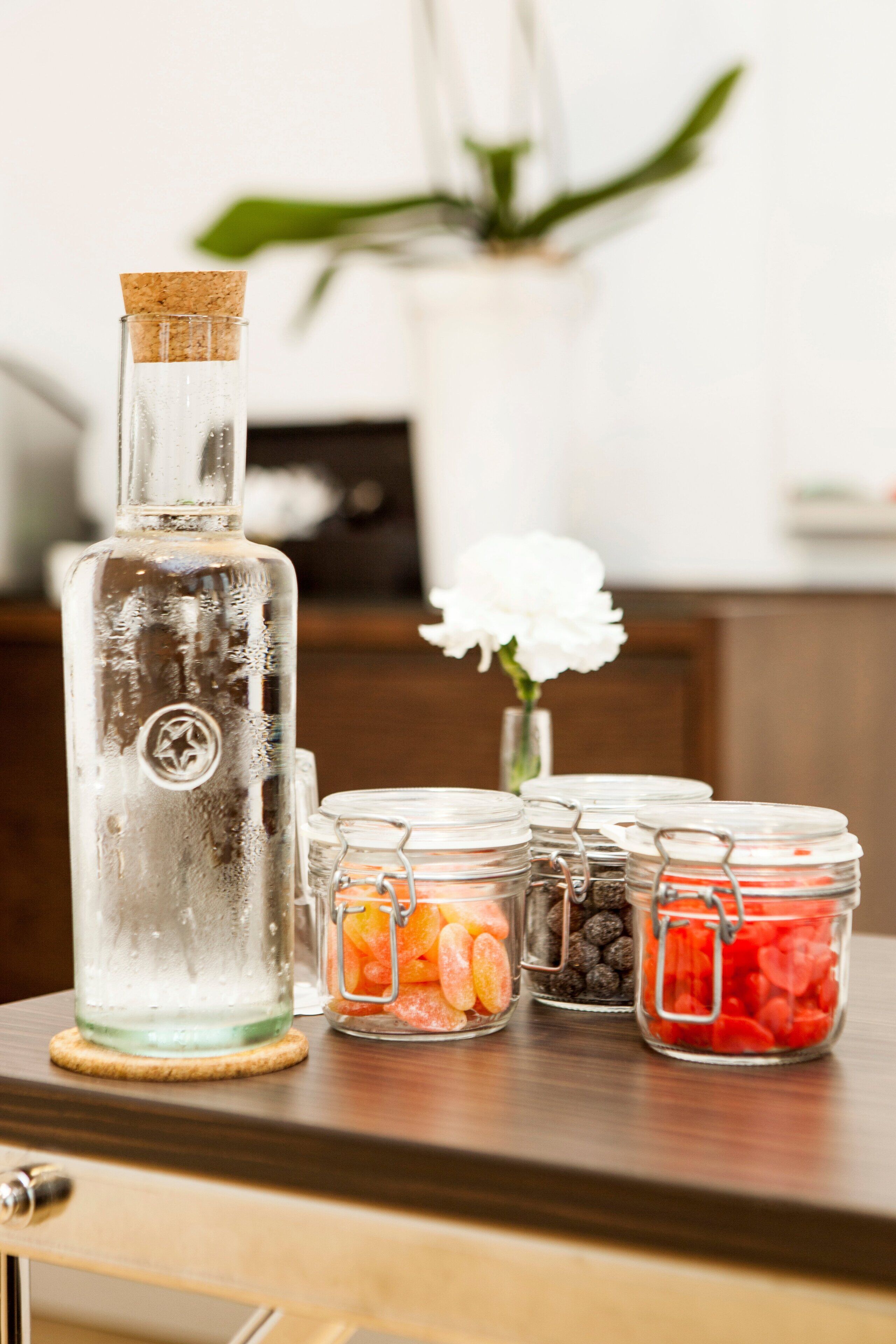 A bottle of clear liquid with a cork stopper, surrounded by glass jars containing various items.