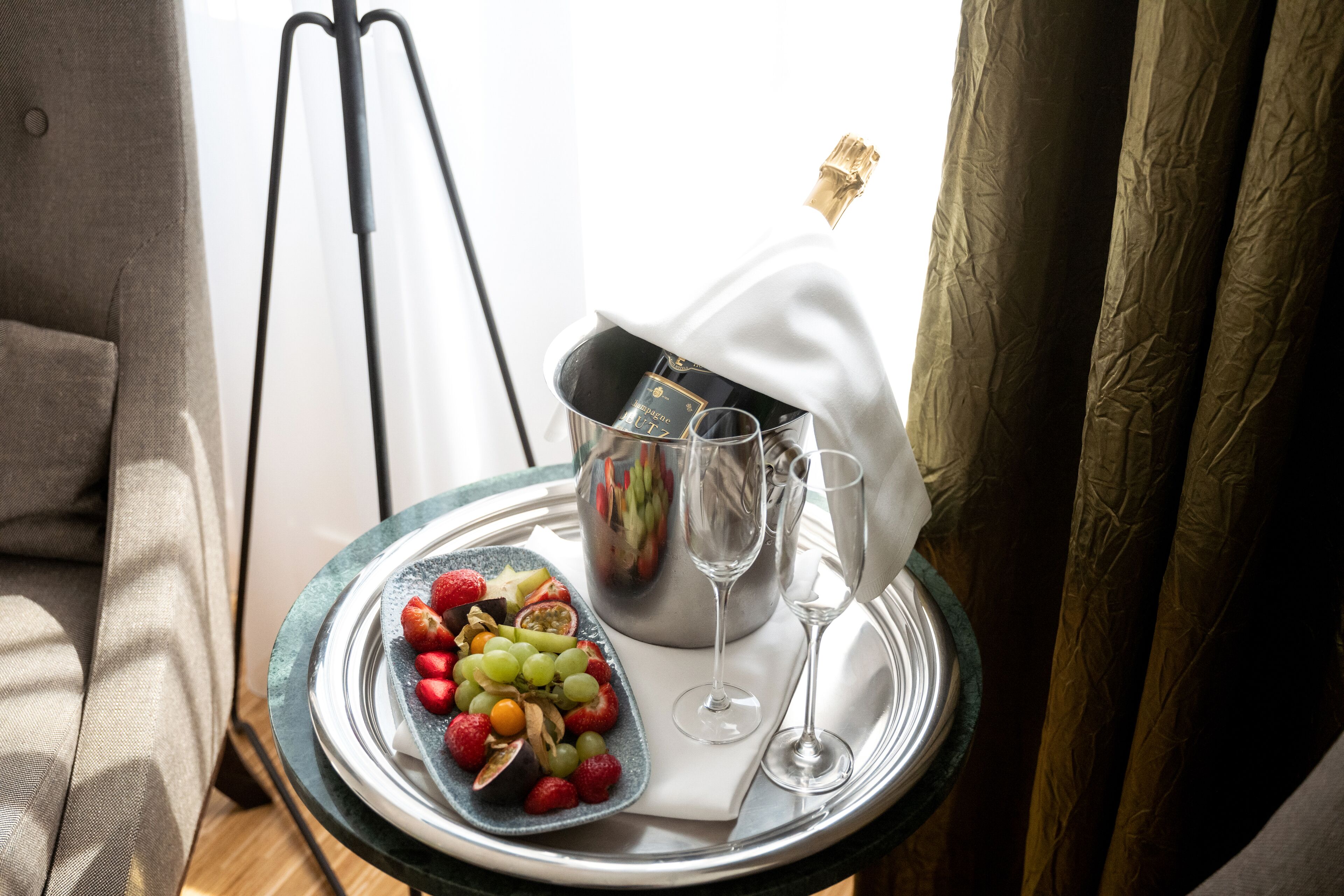 Uma mesa com uma travessa de frutas, um balde de champanhe e duas taças de vinho.