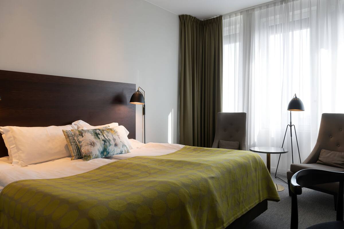 Ett hotellrum med en stor säng, två sänglampor, en stol och ett litet bord.