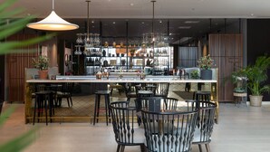 Zona de bar moderna con una barra central, diversas opciones de asientos y una variedad de copas exhibidas en estanterías.