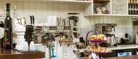 A coffee shop counter with a menu board above, shelves with coffee beans and jars, and a coffee machine.