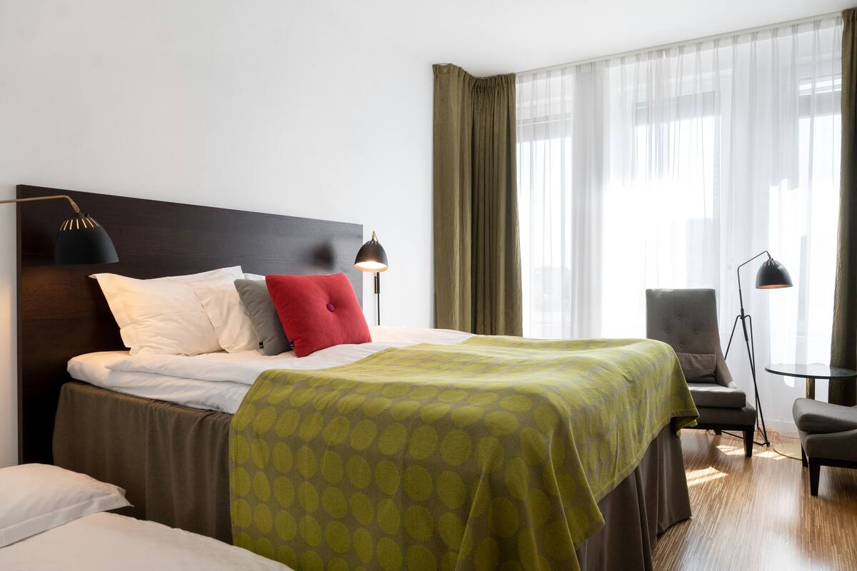 Ett hotellrum med en stor säng, två sänglampor, en stol och ett litet bord.