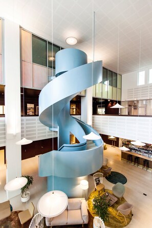 En modern inredning med en blå, spiralformad trappa, sittgrupper och en bar/lounge med högt i tak och stora fönster.