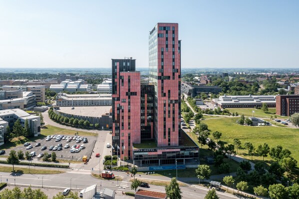 Ett modernt hotell med en iögonfallande röd och svart fasad, omgivet av en parkeringsplats och grönområden.