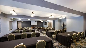 A conference room with multiple tables and chairs, equipped with ceiling lights and a projector screen.