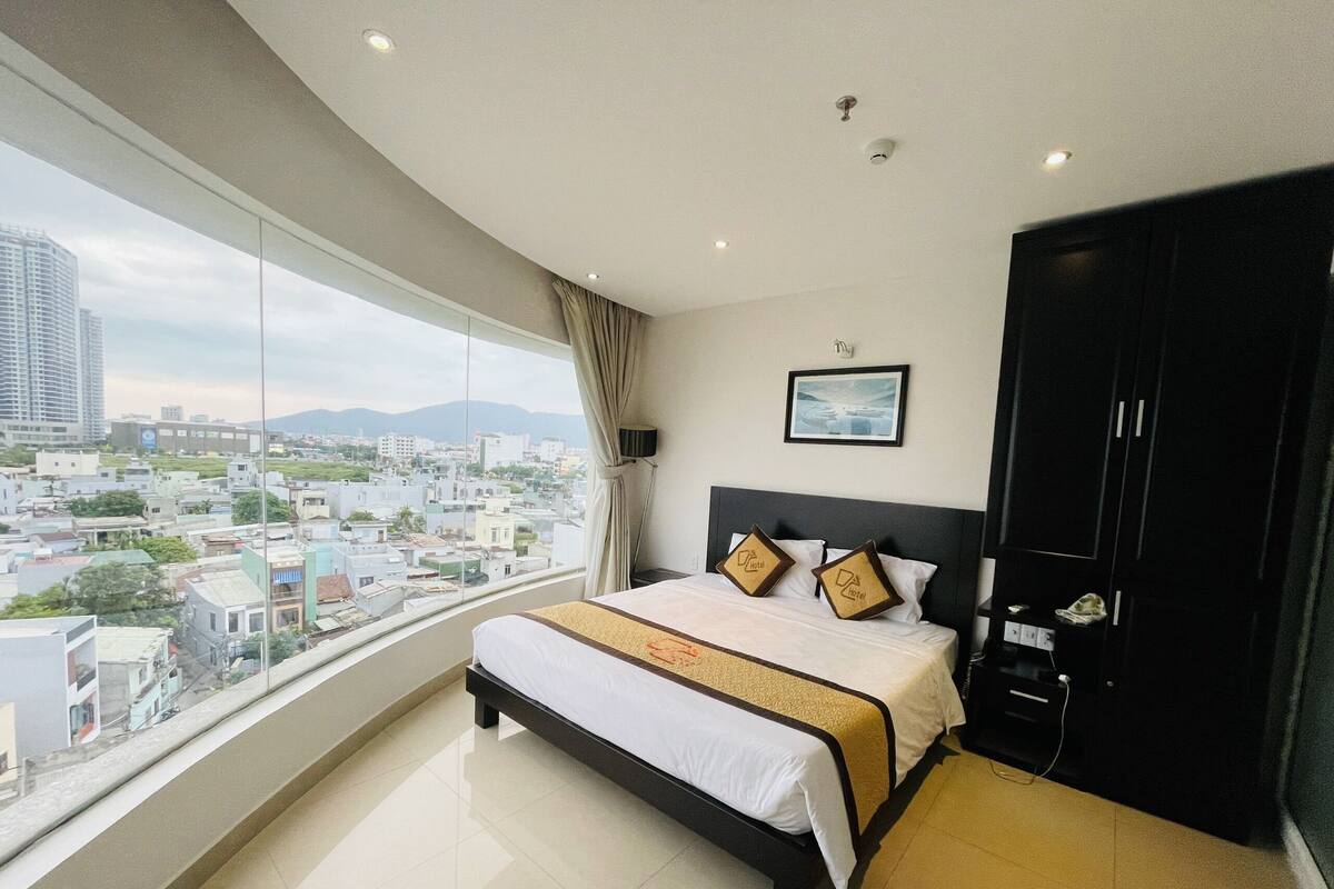 Une chambre d’hôtel moderne, dotée d’un grand lit, d’une armoire et offrant une vue sur le paysage urbain.