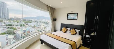 A modern hotel room with a large bed, a wardrobe, and a view of the cityscape.