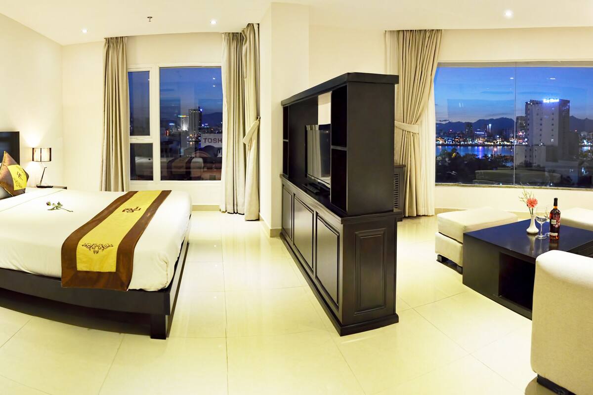 Une chambre d’hôtel moderne dotée d’un grand lit, d’une télévision, d’un bureau et offrant une vue sur le paysage urbain.