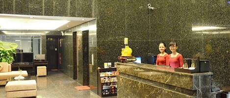 A reception area with a marble reception desk, a large potted plant, and a television.