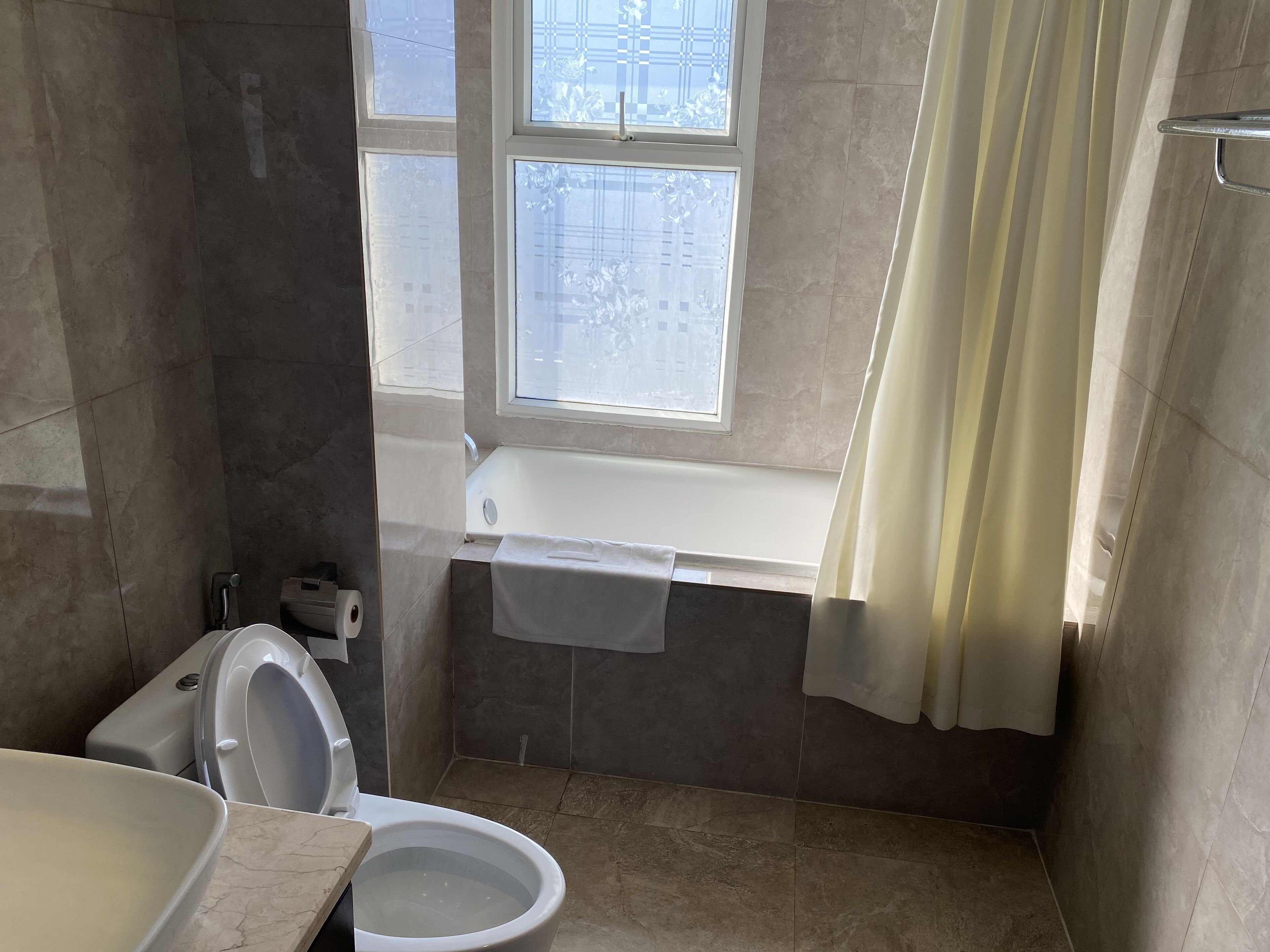 A bathroom with a toilet, a sink, a bathtub, and a window with curtains.