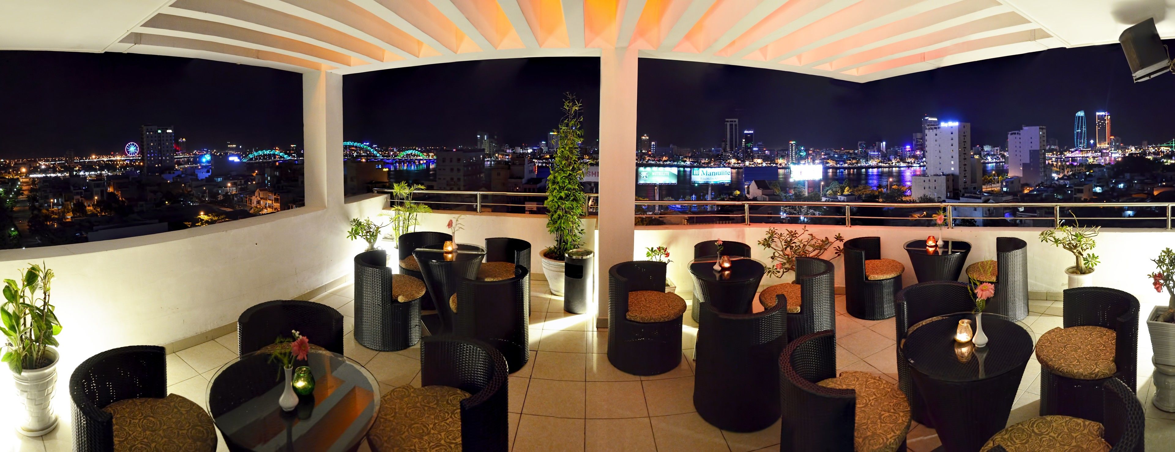 Terraza en la azotea con mobiliario exterior, plantas en macetas y vista panorámica de la ciudad de noche.