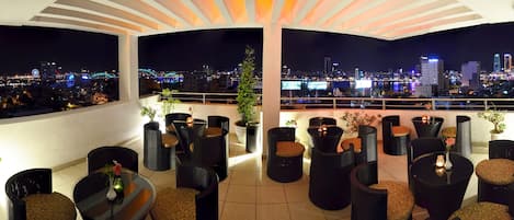 Terraza en la azotea con mobiliario exterior, plantas en macetas y vista panorámica de la ciudad de noche.