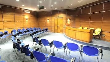 Uma sala de conferências com fileiras de cadeiras azuis, um púlpito de madeira e piso coberto de carpete.