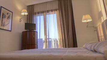 A hotel room with a bed, a television on a wooden cabinet, and two wall-mounted lamps.
