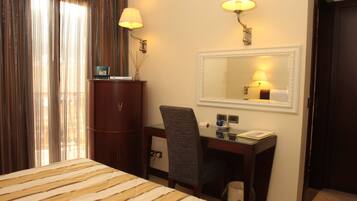 A hotel room with a bed, desk, chair, lamp, mirror, and a wardrobe.