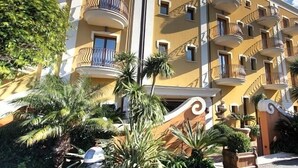 A multi-story hotel with balconies, palm trees, and a decorative entrance. - Cala del Porto (Vibo Valentia)