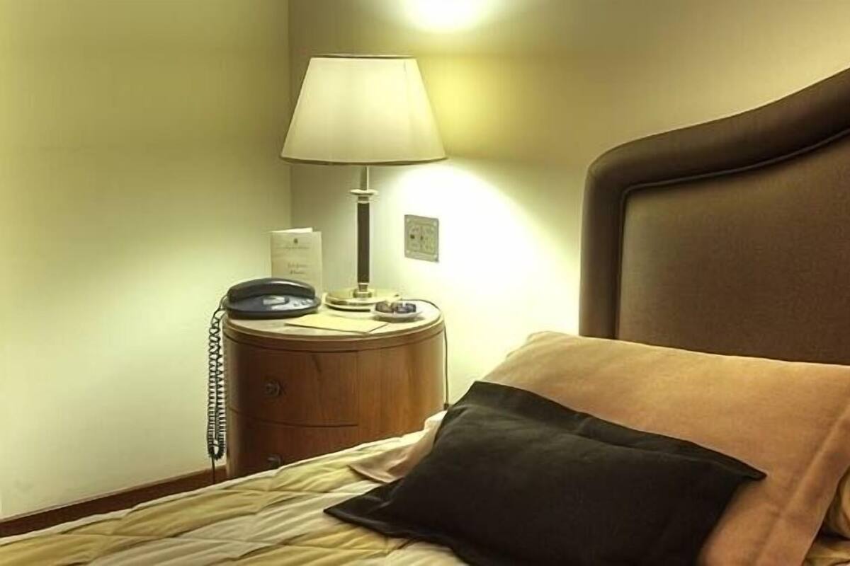 A hotel room with a bed, a bedside lamp, a telephone, and a nightstand.