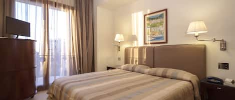 Une chambre d’hôtel avec un grand lit, deux lampes de chevet, un téléviseur à écran plat, une armoire en bois et un tableau au mur.