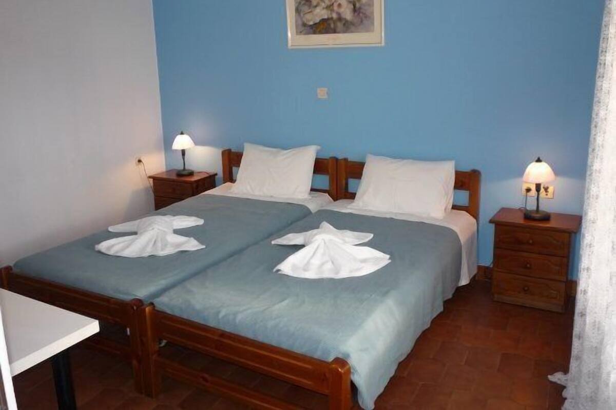 A double bed with two white towels, a wooden headboard, two bedside tables with lamps, and a painting on the wall.