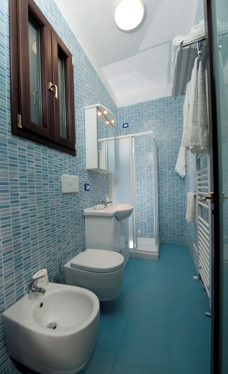 A bathroom with a bidet, a toilet, a sink, and a glass-enclosed shower.