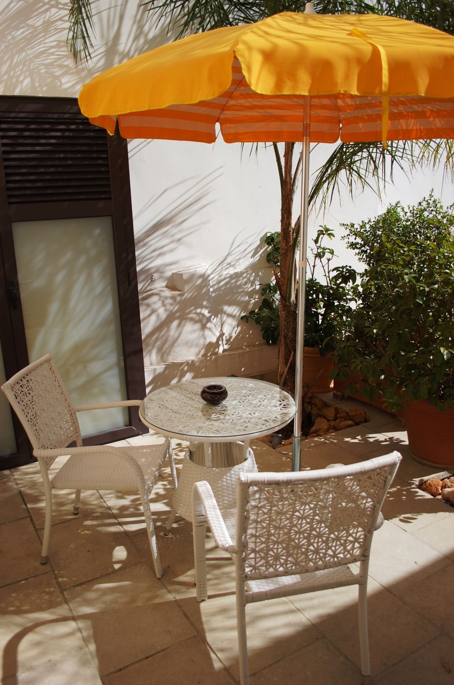 A patio area with a round table, two white wicker chairs, and a yellow umbrella.