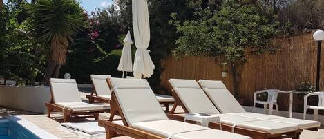 A poolside area with wooden lounge chairs and white umbrellas.