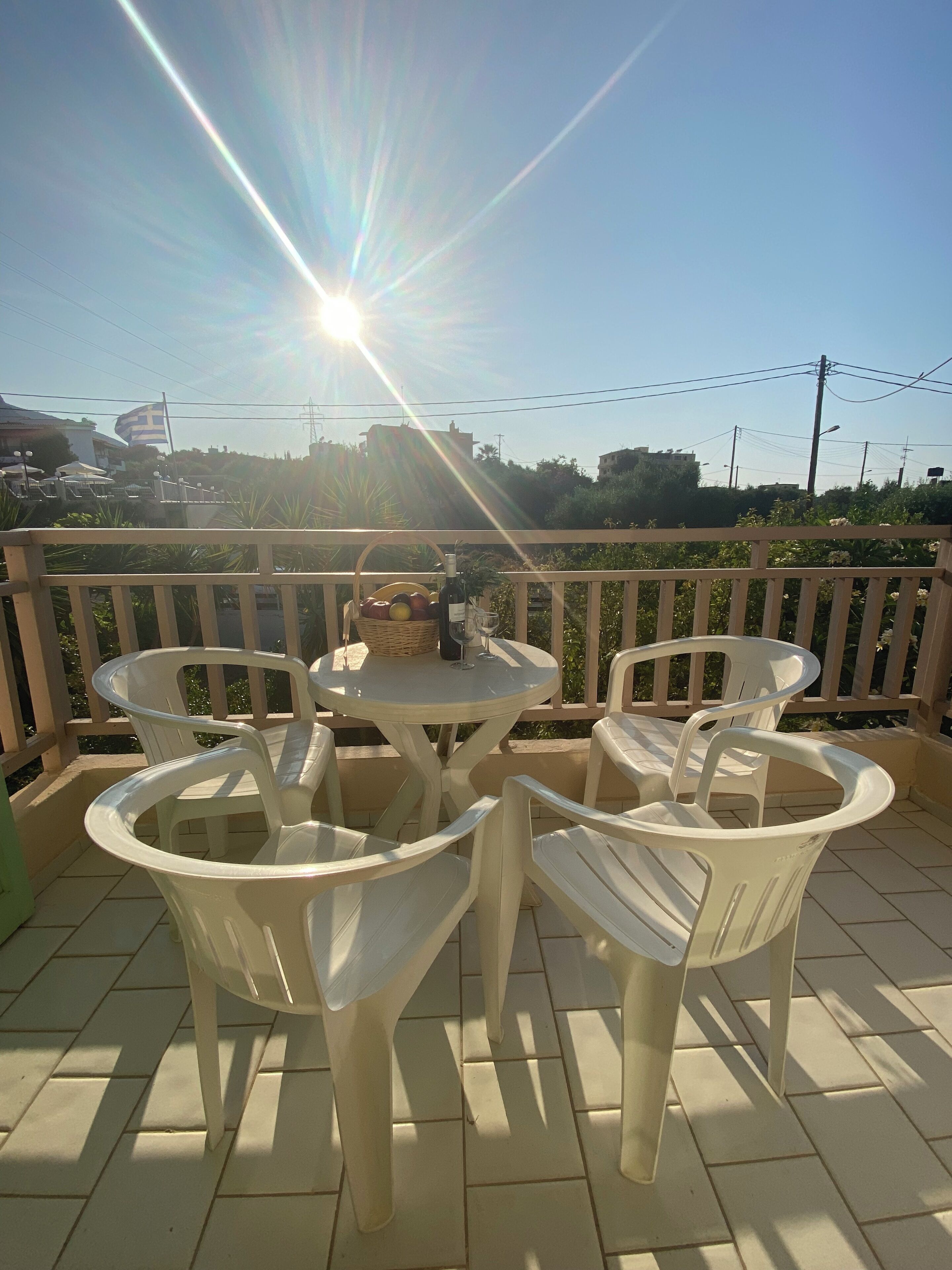 A balcony with plastic chairs and a table, a bottle, and a basket of fruit.