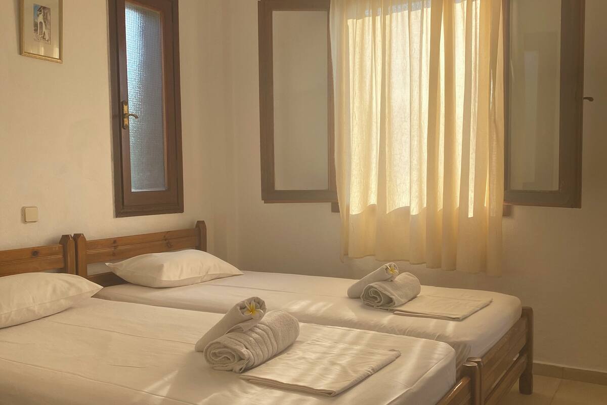 A double bed with wooden headboards, two bedside tables, and a large window with curtains.