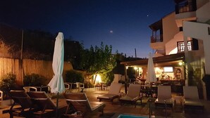 A pool area with lounge chairs and umbrellas, a bar area with tables and chairs, and a building with a balcony. - Sirocco Apartments (Hersonissos)