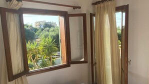 A bedroom with two beds, a window with curtains, a mirror, and a view of greenery outside. - Sirocco Apartments (Hersonissos)
