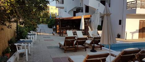 A poolside area with lounge chairs and umbrellas, a bar, and a staircase leading to an upper floor.
