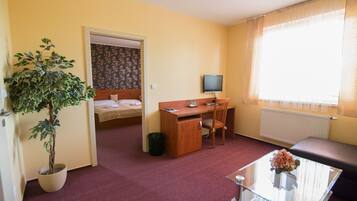 A hotel room with a bed, a desk, a chair, a TV, a potted plant, and a window with curtains.