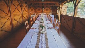 Una larga mesa dispuesta para una comida en una habitación rústica de madera con techos altos y luz natural.