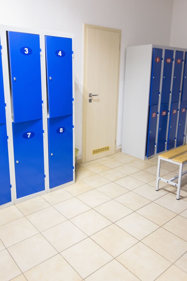 A locker room with blue lockers numbered 3 to 11, a wooden bench, and a beige tiled floor.